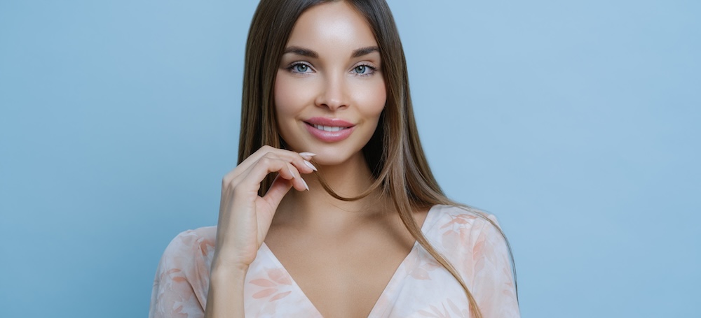 Portrait of beautiful dark haired woman smiling against blue backdrop.