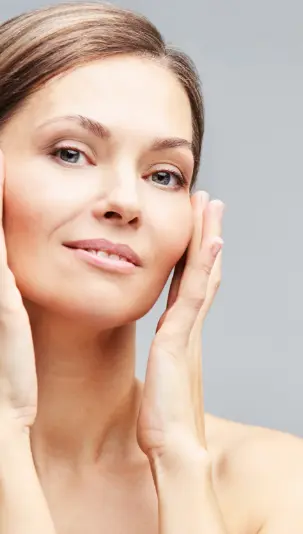 Skin Tightening: An older caucasian woman with clear skin has her hands on her cheekbones.