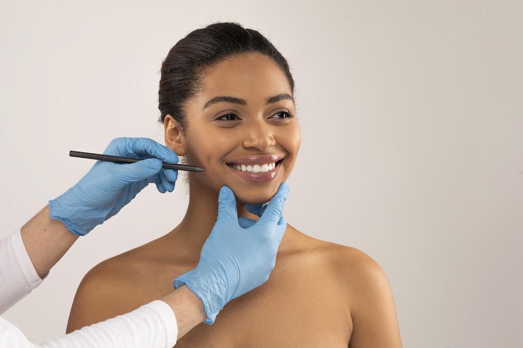Young woman smiling while plastic surgeon assesses her chin for possible surgery.