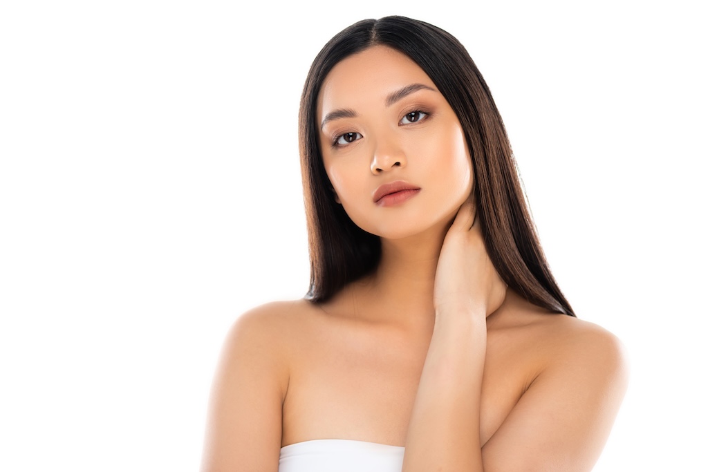 brunette woman looking at camera while touching neck isolated on white
