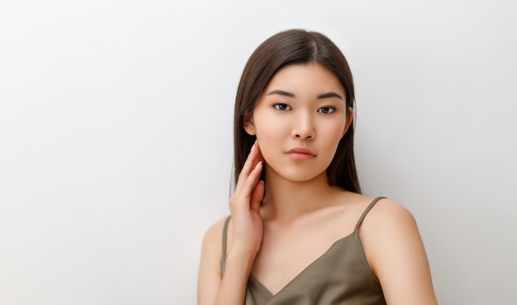 Beautiful asian girl with clean skin, natural makeup on grey background.