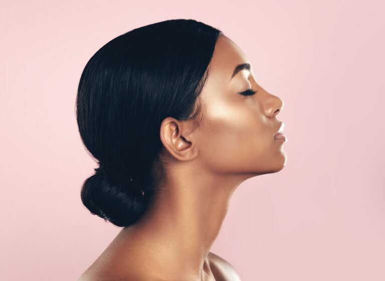 Silhouette of a beautiful young woman posing with her eyes closed against a pink background, emphasizing her side profile and jawline.