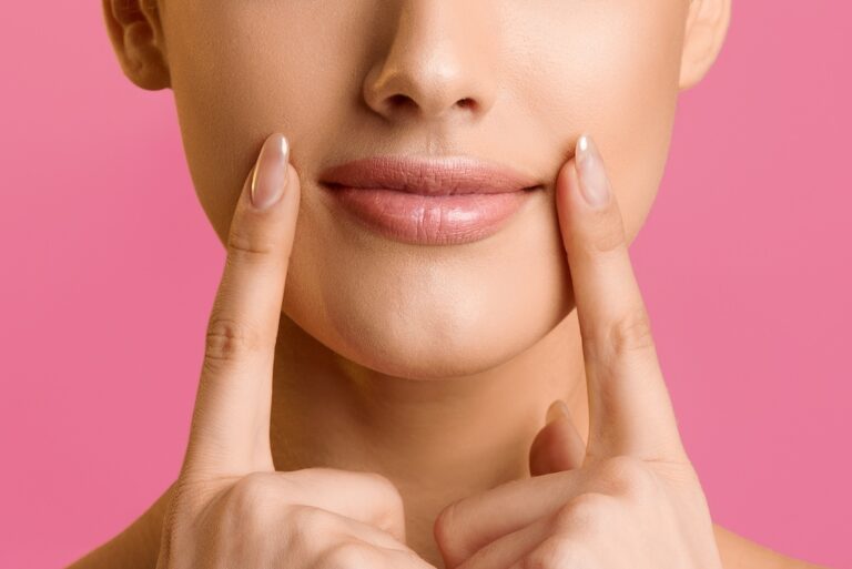 Young woman holding fingers near lips, pink background
