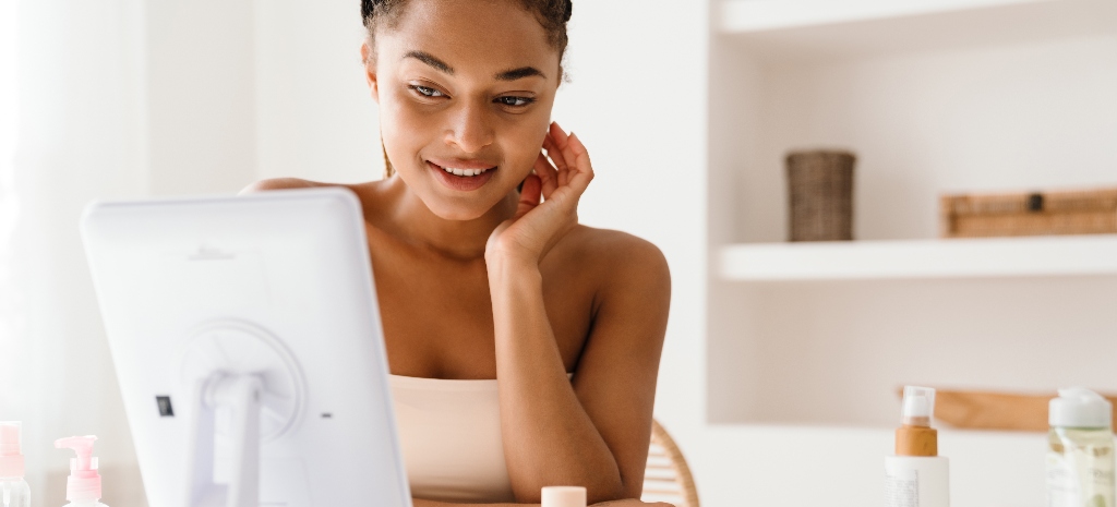 Young woman smiling and looking in mirror while doing virtual beauty consultation