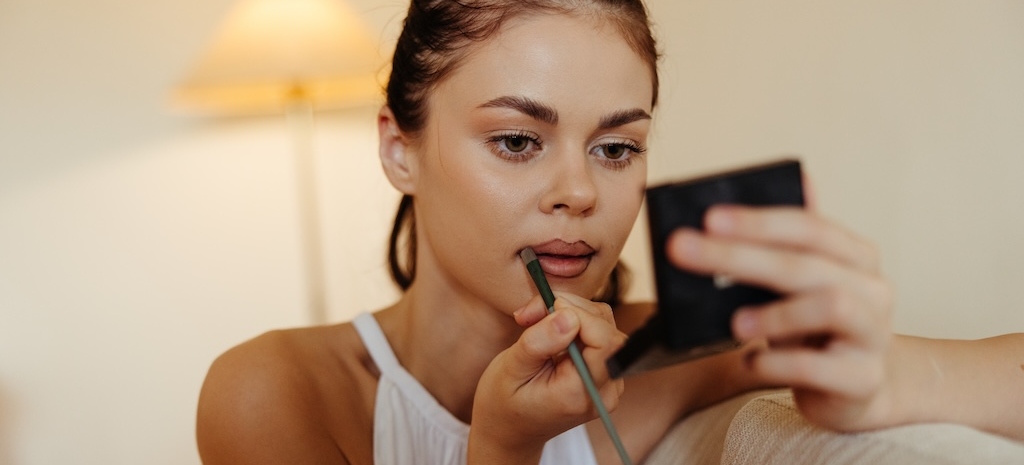 A woman at home looks in the mirror and applies natural-looking makeup
