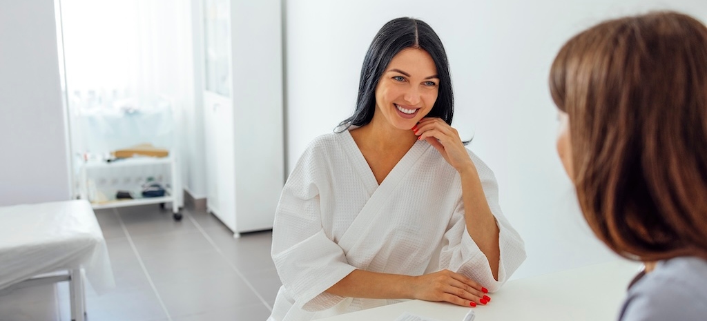 Young woman sitting in consult with woman in plastic surgery office.
