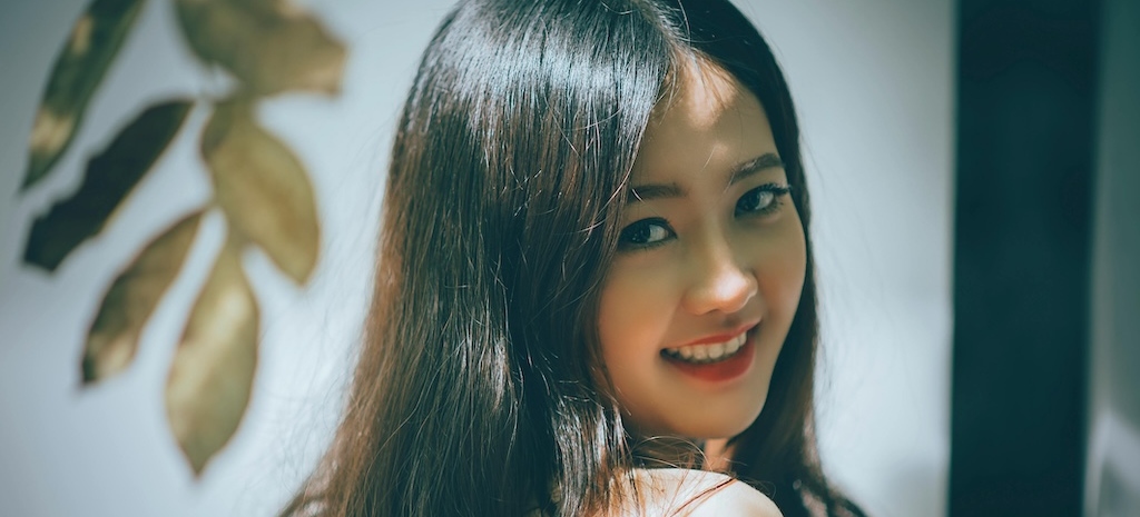 Young woman looking over her shoulder into the camera, smiling, with a plant in the background