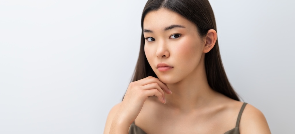 Beautiful asian girl with clean skin, natural makeup on grey background.