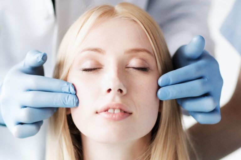 Beautiful woman at plastic surgery consultation, surgeons gloves analyzing her facial structure.